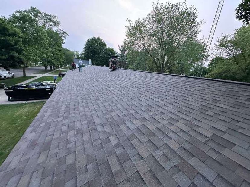 Roof installation in progress on a residential building with trees in the background.